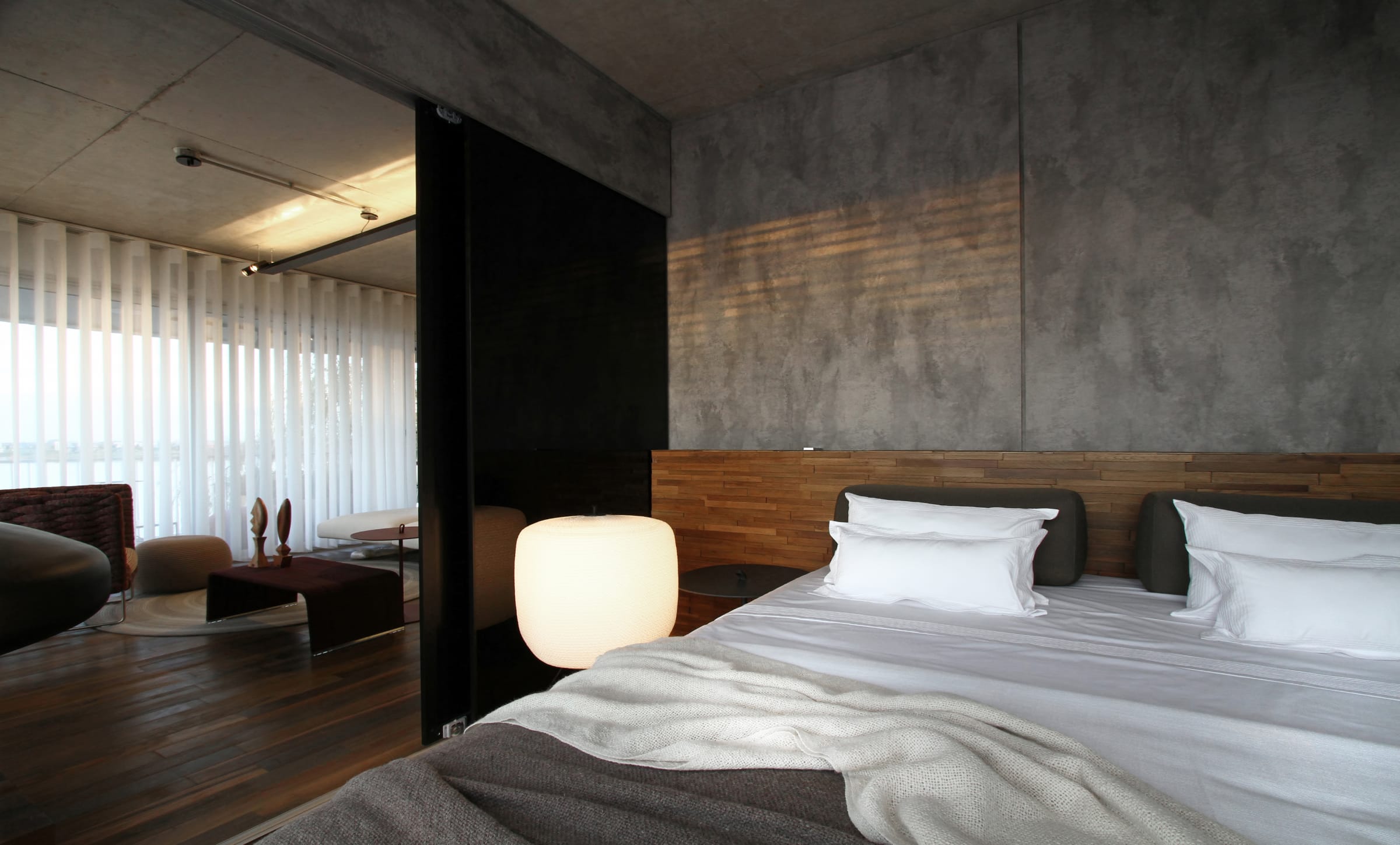Paneles de vidrio negro integran el dormitorio con el living. Piso de palo Santo (Patagonia Flooring) y paredes revestidas con panel modelo Street, simil cemento (Faplac).