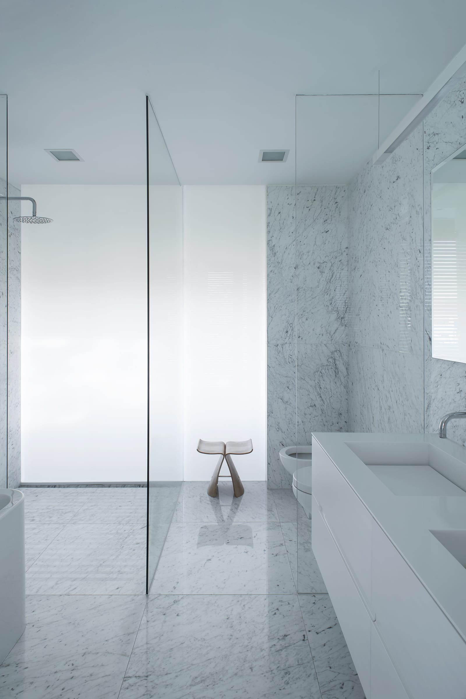 Una pared de vidrio blanco lleva luz natural difusa al interior de los baños.